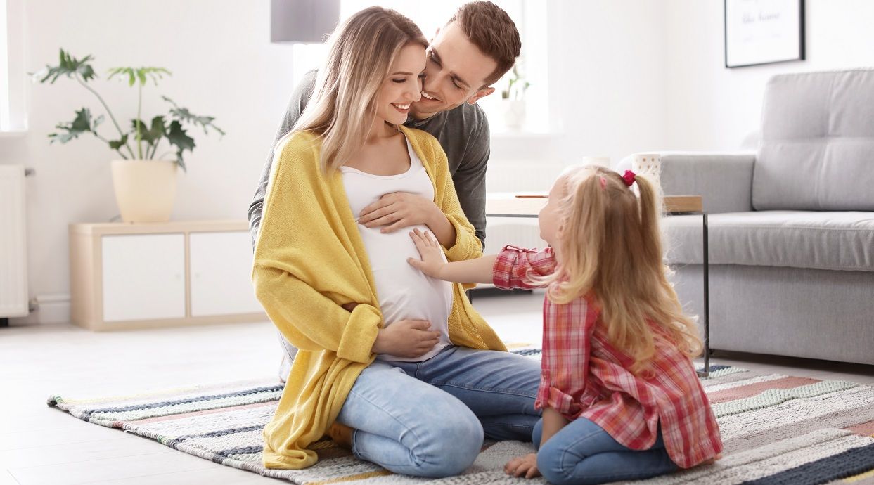 Frau im 6. Schwangerschaftsmonat mit Mann und Tochter