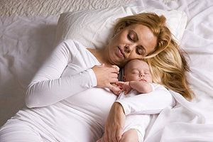 Ein Mutter liegt mit ihrem Baby im Wochenbett