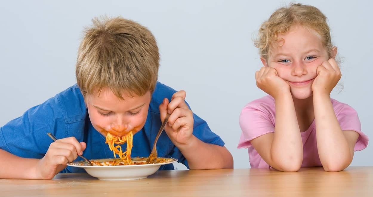 Kindern Benehmen beibringen: Junge isst Nudeln, Mädchen sieht zu