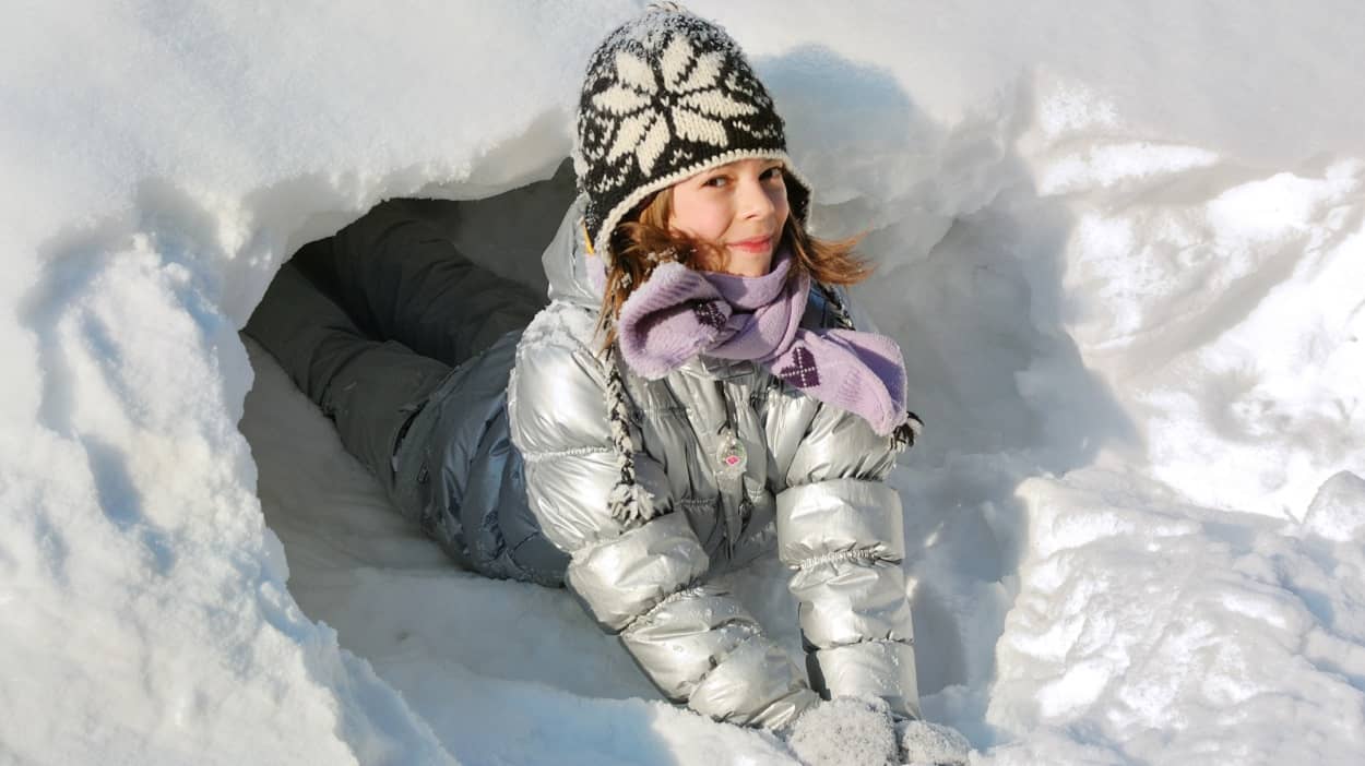 Mädchen liegt in ihrer Schneeburg