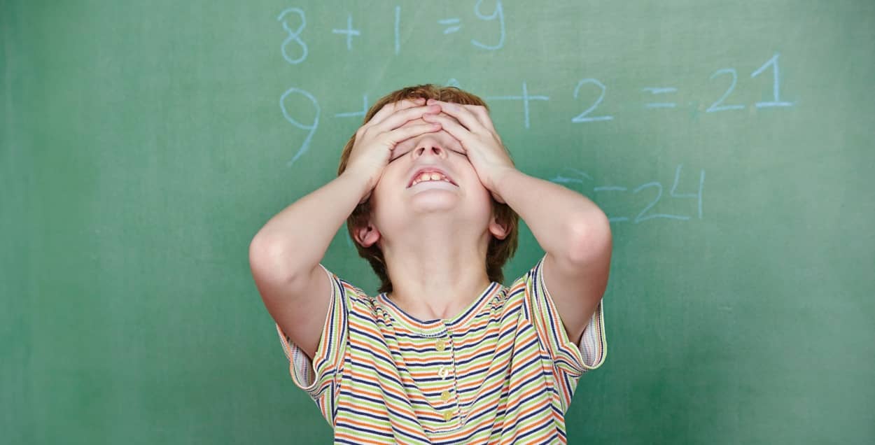 Junge mit Dyskalkulie steht vor einer Tafel mit Matheaufgaben